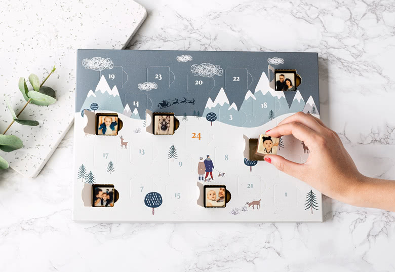 Calendrier de l'Avent chocolat personnalisé avec un design de montagne d'hiver, avec des emplacements pour photos derrière des portes numérotées pour chaque jour de décembre.