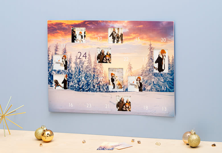 Personalised photo advent calendar with a snowy forest scene and sunset background, featuring custom photos behind numbered doors.