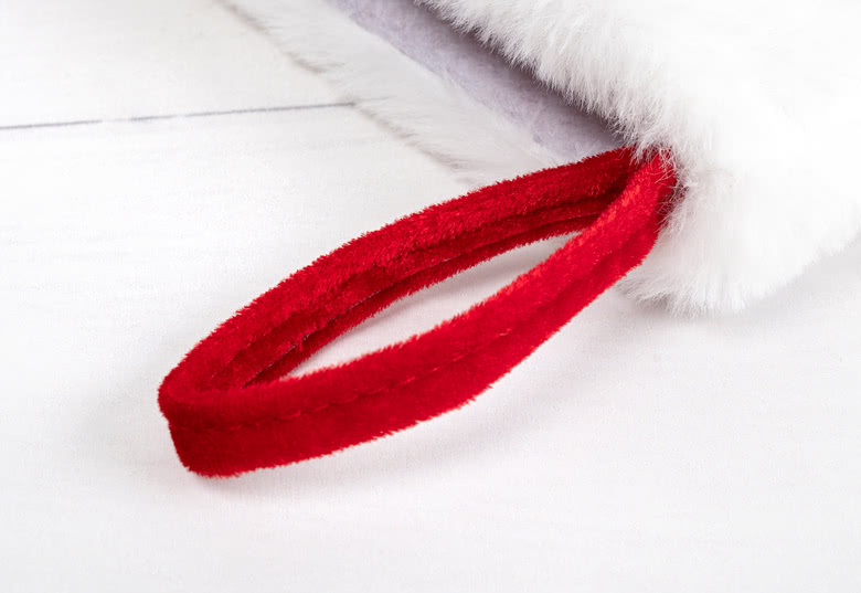 Gros plan d'une chaussette de Noël blanche avec une texture douce et pelucheuse, avec une boucle de suspension rouge pour un affichage facile.