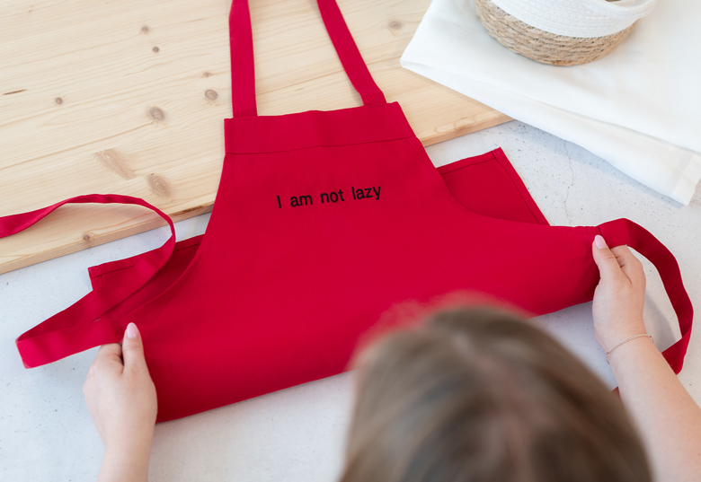 Rødt børneforklæde med "I am not lazy" tekst i sort på forsiden.