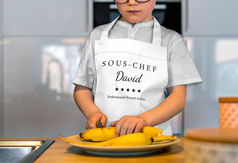 Valkoinen lasten esiliina, jossa henkilökohtainen "SOUS-CHEF David" -teksti ja "Professional dessert tester" -teksti.