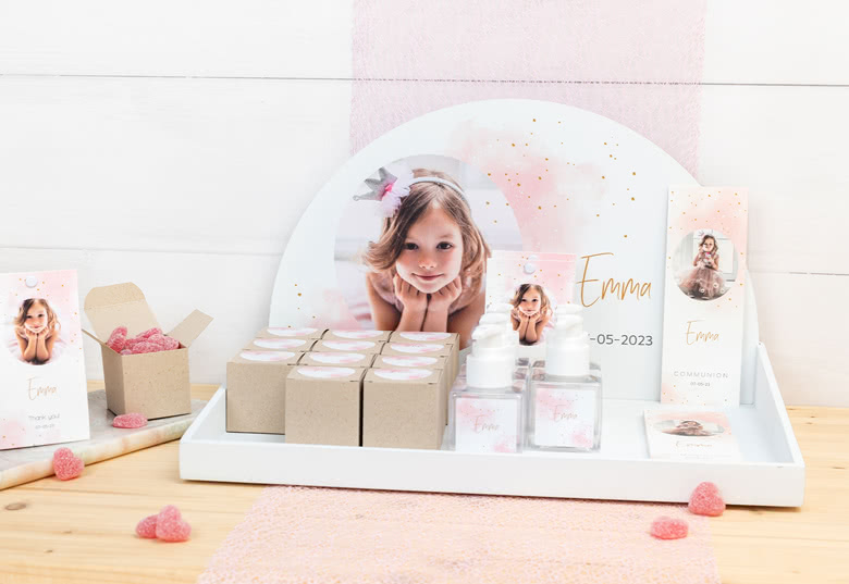 Personalised favour display featuring a photo of a girl named Emma. Includes small boxes, hand sanitiser bottles, & thank you cards.