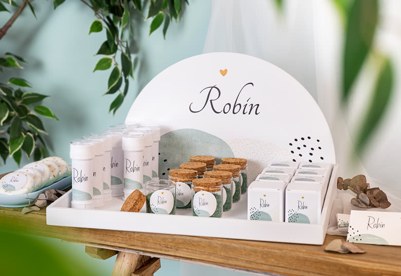 Personalised favours display with white & green theme, featuring custom-labelled bubbles, jars with cork lids, & small boxes.