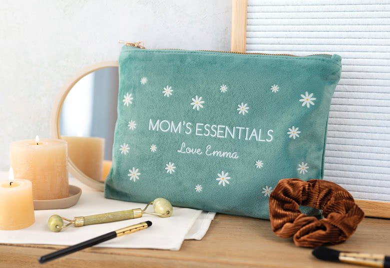 Green velour toiletry bag with white daisy patterns, personalised with "MOM'S ESSENTIALS" and "Love Emma" in white text.