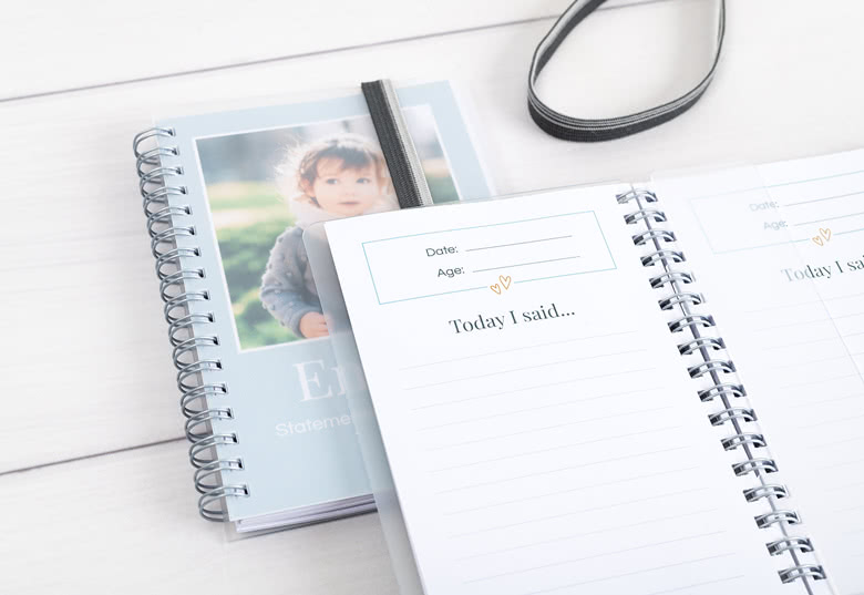 Personalisierte spiralgebundene Notizbücher mit einem hellblauen Umschlag, der ein Kinderfoto und Platz für das Datum und Alter zeigt. Die Innenseiten haben linierte Abschnitte mit der Überschrift "Today I said...".