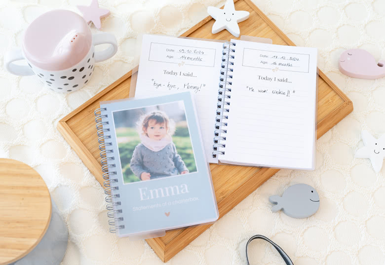 Personalised spiral-bound notebooks with "fill in the blanks" sections, featuring a baby photo and "Emma" on the grey cover.