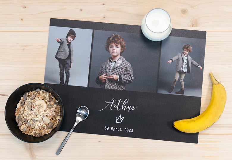 Gepersonaliseerde zwarte placemat met drie fotopanelen en witte tekst 'Arthur, 30 April 2023'.