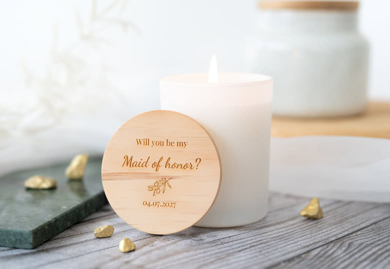 White personalised scented candle with a wooden lid engraved with "Will you be my Maid of honor?" and a date.