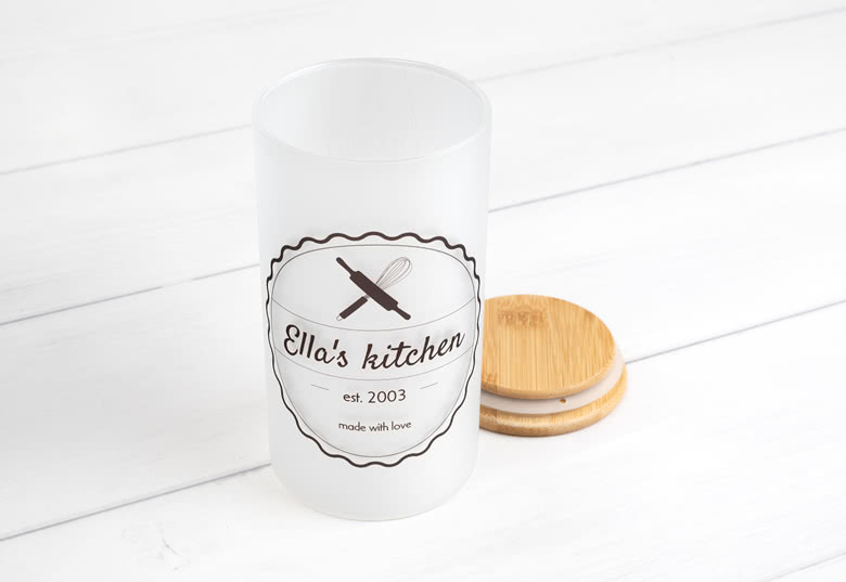 Bocal de rangement blanc personnalisé avec couvercle en bois, présentant le texte "Ella's kitchen" et des graphiques d'ustensiles de cuisine en noir.