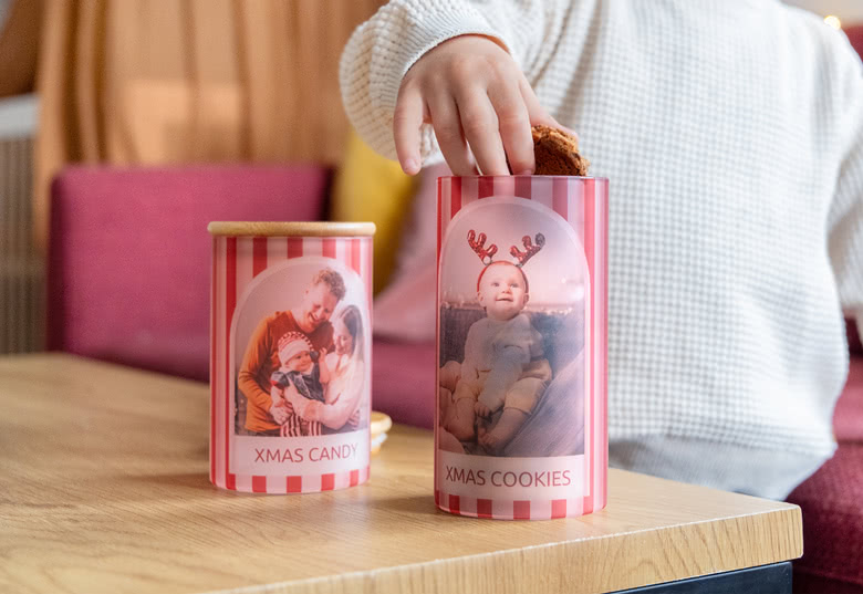 Gepersonaliseerde rood-wit gestreepte voorraadpotten gelabeld "Xmas Candy" en "Xmas Cookies" met aangepaste foto's op een houten tafel.