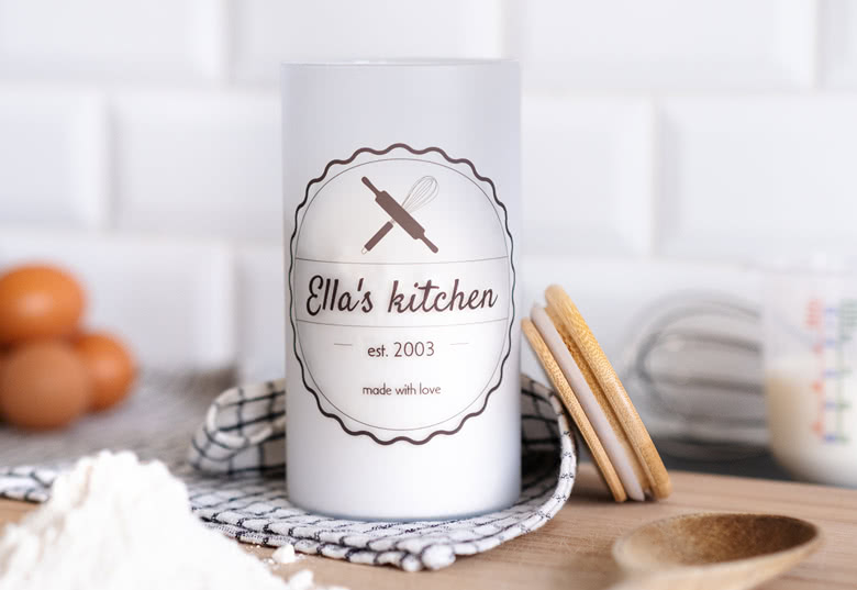 Gepersonaliseerde witte voorraadpot met de tekst "Ella's kitchen" en een afbeelding van keukengerei. Aanpasbare details omvatten naam en jaar.