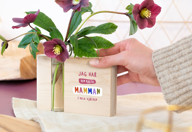 Träblock med glasvas och blommor, med meddelandet "Jag har den bästa mamman i hela världen" i färgstark text, till mors dag.